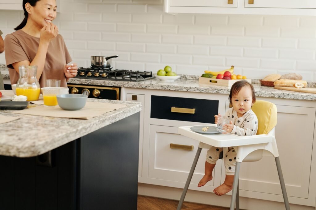 ebê sorridente sentado no cadeirão iniciando a introdução alimentar com as mãos sujas de fruta